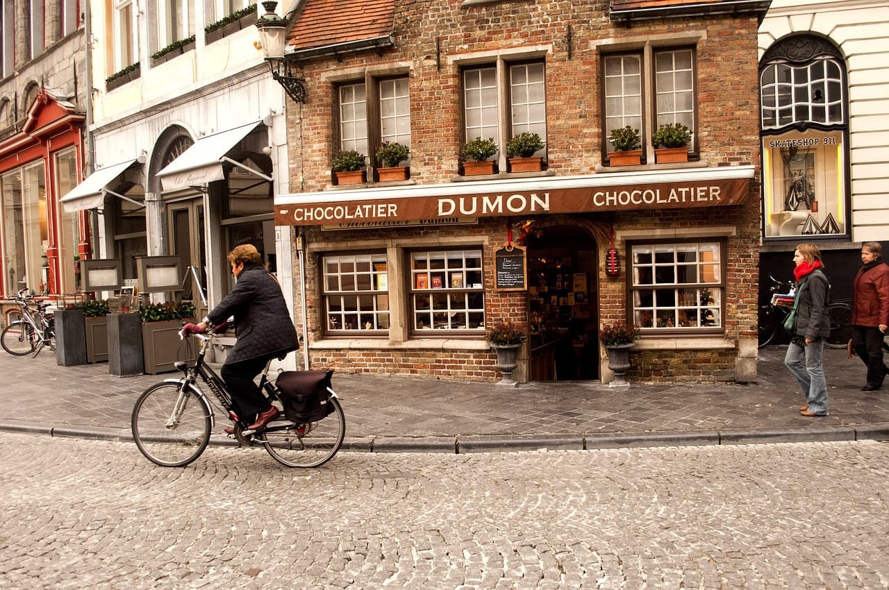 A chocolate shop in Bruges with a man on a bike riding by.